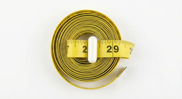 Minimalist photography of a yellow measuring tape coiled around a white 5-HTP capsule, symbolizing the weight loss and appetite suppression benefits of the supplement.